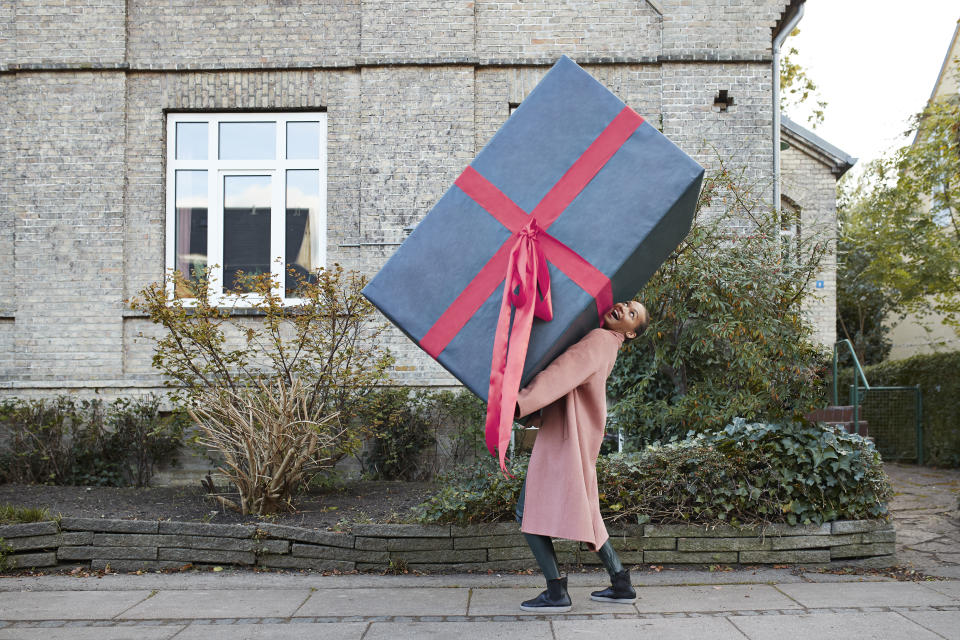 Happy young woman carrying large gift box on footpath