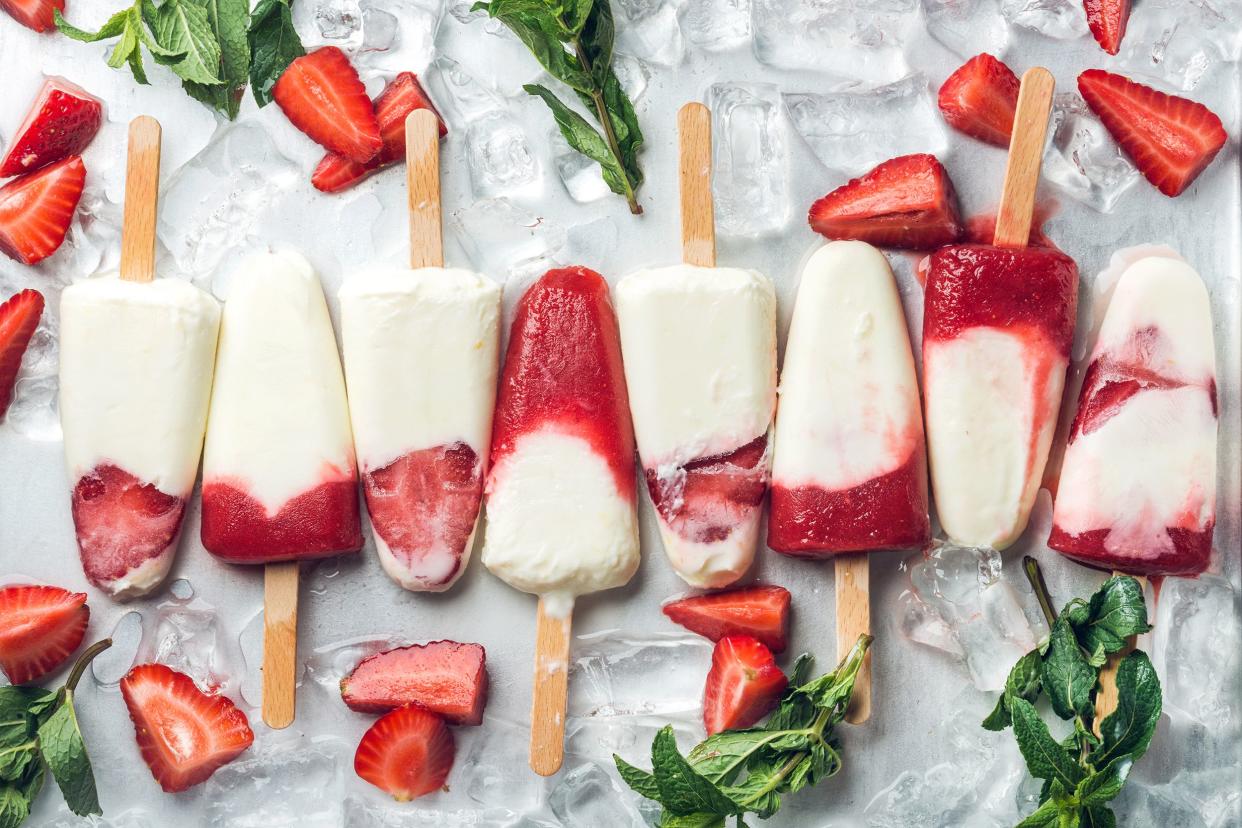 Several strawberry frozen yogurt fruit pops in a line with a background of ice, strawberries, and leaves