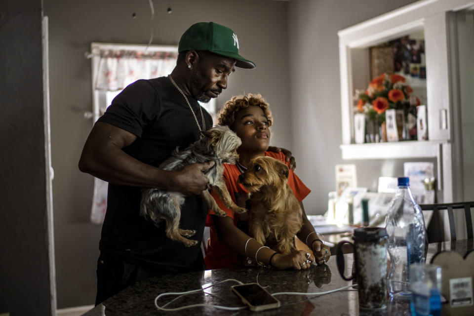 Navada Gwynn, left, embraces his daughter, also named, Navada, 15, as they hold their dogs, Whoa-Whoa, left, and Honey at their home in Louisville, Ky., Monday, Aug. 28, 2023. The Gwynns have pulled their youngest child, Navada, out of school, home schooling to keep her safe. (AP Photo/David Goldman)