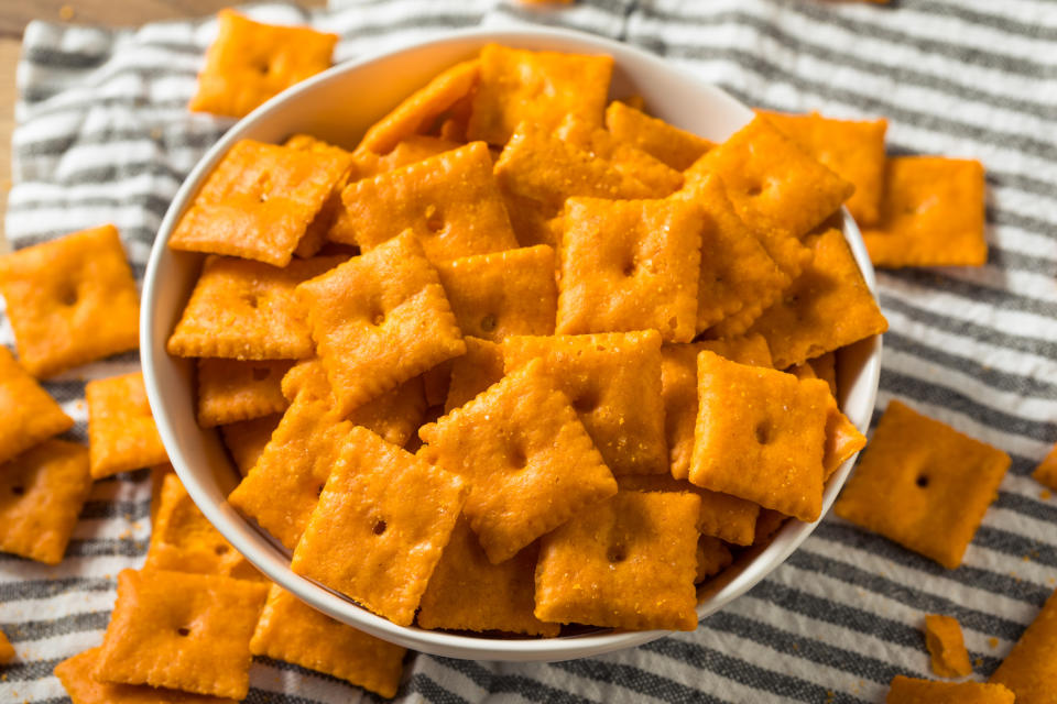 A bowl of square cheese crackers on a striped cloth