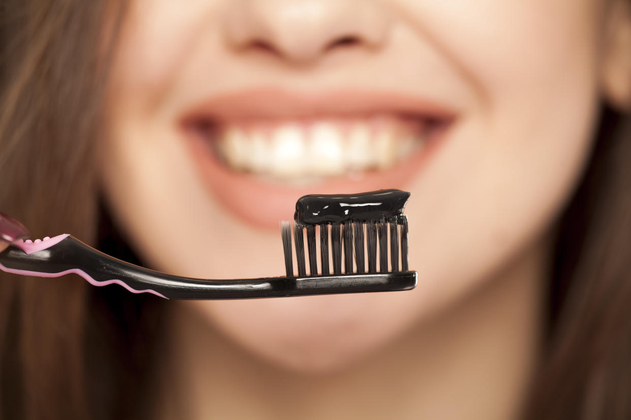 Black toothpaste on a toothbrush. Girl in background.