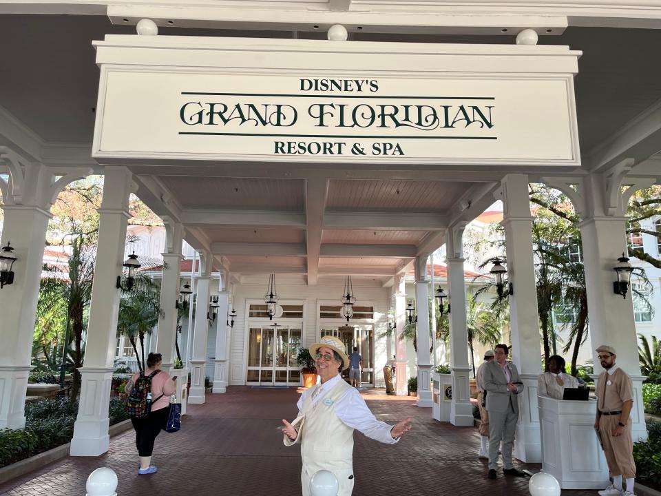 disney cast memeber randy posing for a photo under the grand floridian entrance sign at the front door of the resort