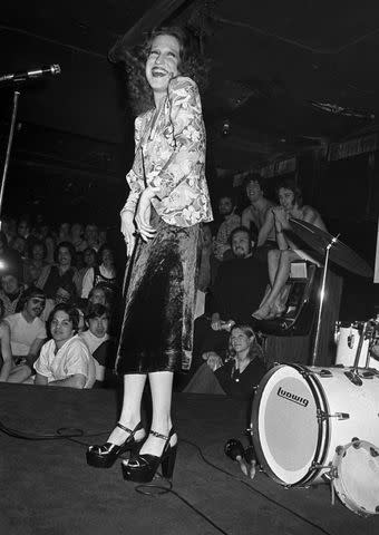 <p>Pierre Venant/WWD/Penske Media via Getty</p> Actress and singer Bette Midler, wearing a velvet skirt and platform shoes, performing for a crowd of gay men at the Continental Club bath house in New York City.