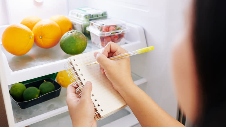 Woman taking notes in front of refrigerator 