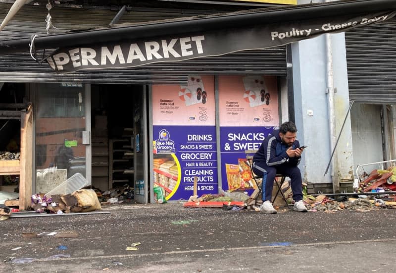 Abdelkader Mohamad Al Alloush, owner of the Sham Supermarket sits outsude his destroyed shop on Donegall Road in Belfast. The shop was burned during disorder in the area following an anti-immigration protest on Saturday. Another attempt was made to burn it during the disorder on Monday night. Rebecca Black/PA Wire/dpa