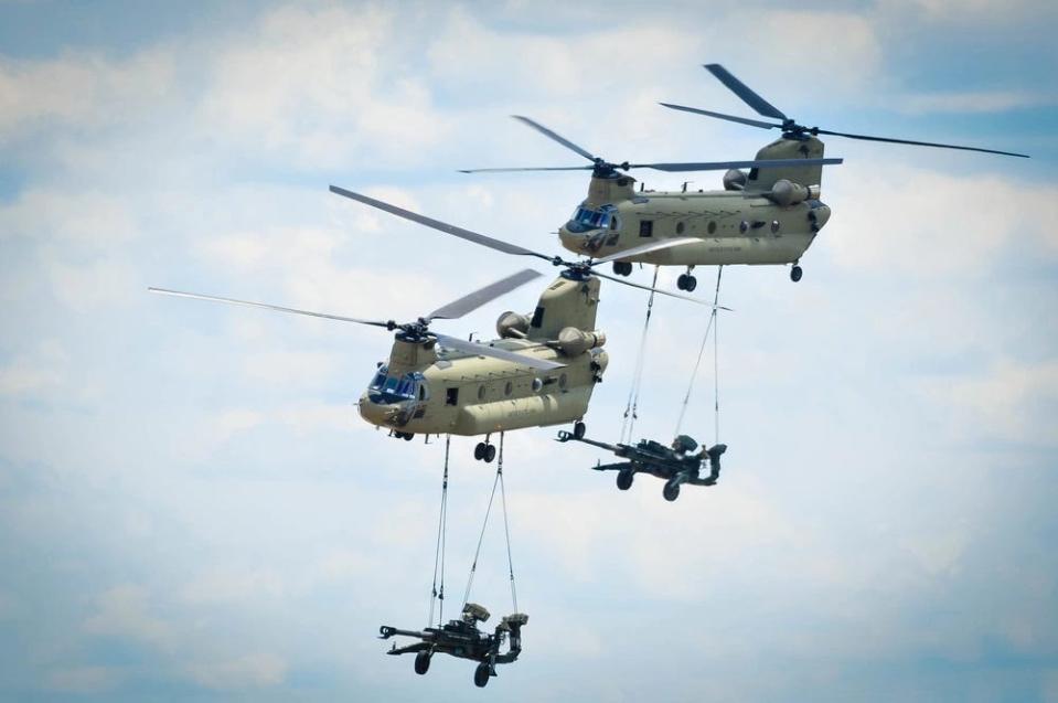 Two CH-47 Chinook helicopter’s assigned to 3rd General Support Aviation Battalion, 82nd Combat Aviation Brigade, 82nd Airborne Division perform tactical maneuvers to place two M777A2 Howitzers in position for onlookers  during the 2017 All American Week Airborne Review on Sicily Drop Zone at Fort Bragg.