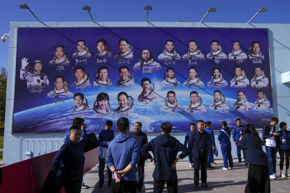 Staff members gather near a billboard depicting Chinese astronauts on the past Shenzhou missions after Chinese astronauts for the upcoming Shenzhou-17 mission met with the press at the Jiuquan Satellite Launch Center in northwest China, Wednesday, Oct. 25, 2023. (AP Photo/Andy Wong)