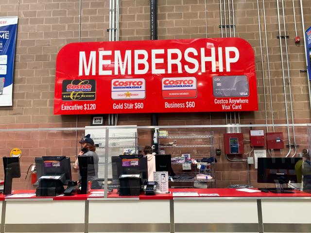 Membership counter at Costco with computers and red sign against brick wall