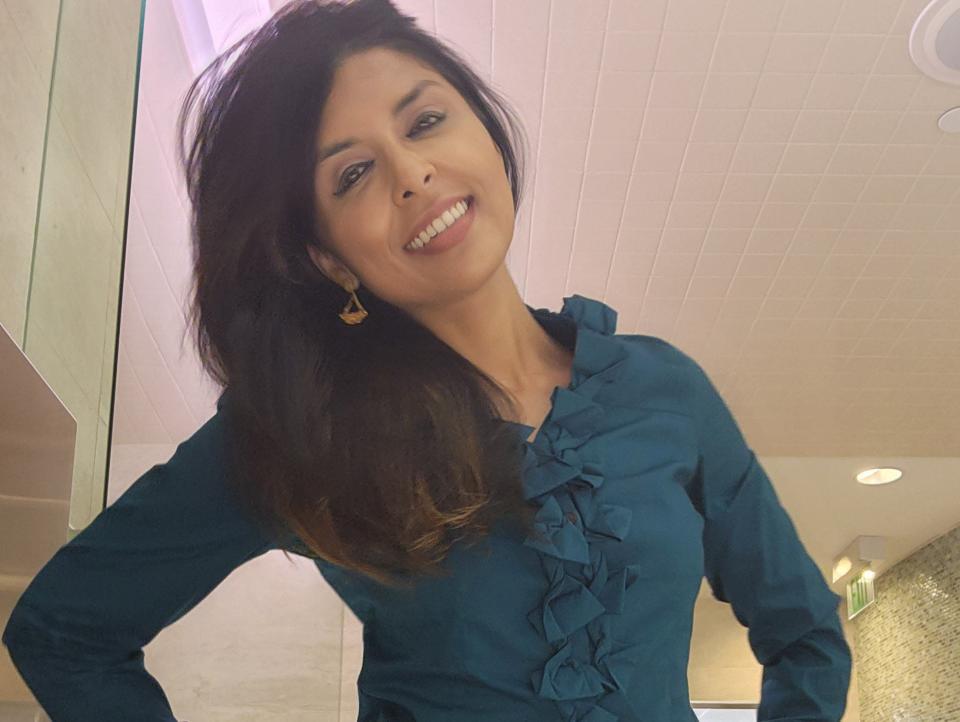 Sonali Chandra, a 35-year-old virgin, poses in a teal blouse and a white skirt. She is standing in the women's locker room of the gym where she works.