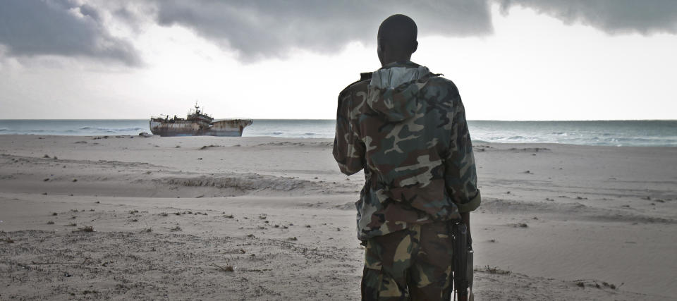 FILE - In this Sunday, Sept. 23, 2012 file photo, a Somali soldier looks out at a Taiwanese fishing vessel that washed up on shore after the pirates were paid a ransom and released the crew, in the once-bustling pirate den of Hobyo, Somalia. World sea piracy fell for a third straight year in 2013, as Somali pirates were curbed by international naval patrols and improved ship vigilance, an international maritime watchdog said Wednesday, Jan. 15, 2014. (AP Photo/Farah Abdi Warsameh, File)