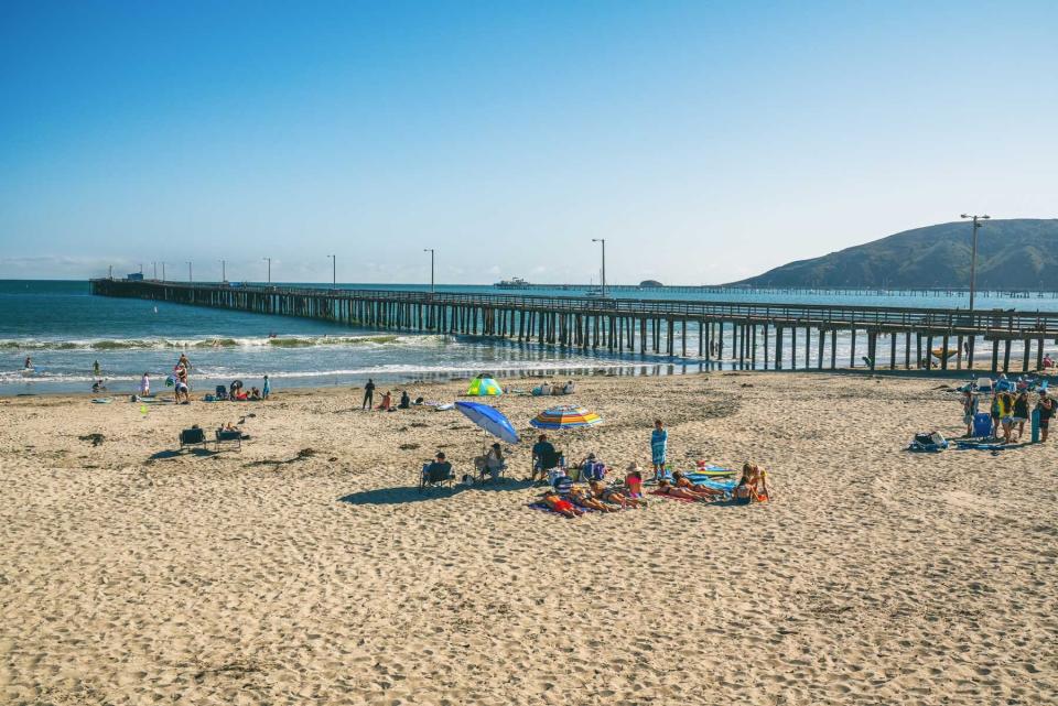 People enjoying Avila Beach near the pier on a sunny blue sky day