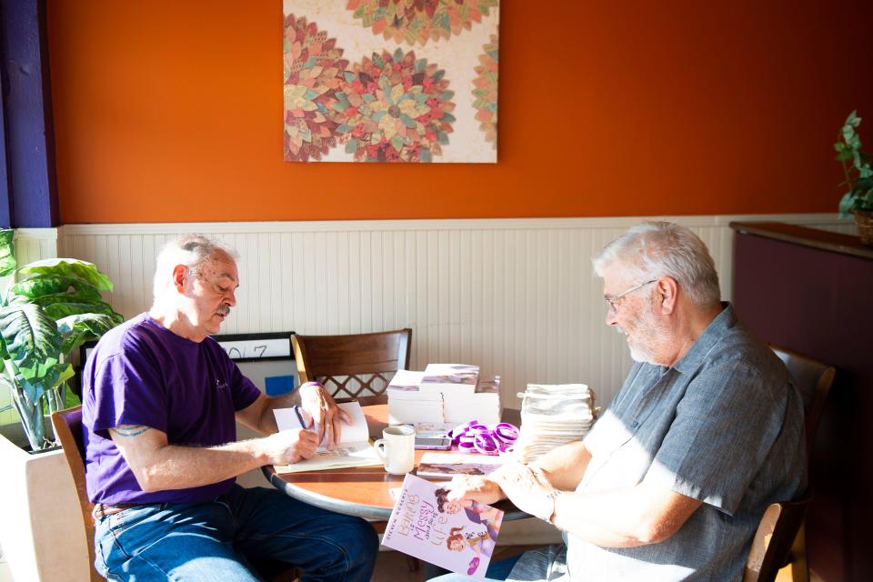 Steven Roberts, author of the book "Baking is Messy And So Is Life," signs a book while chatting with longtime friend Steve Mauney at Rami's Cafe in Knoxville, Tenn. on Wednesday, Aug. 24, 2022. Roberts and Mauney worked many years together for the State of Tennessee.