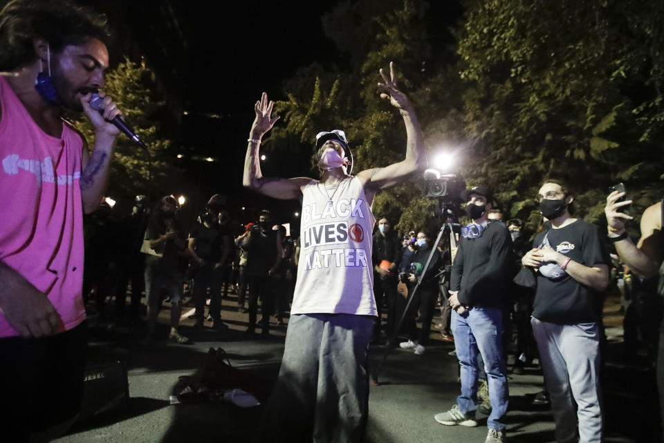 A performer, left, raps as a man dances during a Black Lives Matter protest at the Mark O. Hatfield United States Courthouse Thursday, July 30, 2020, in Portland, Ore. After days of clashes with federal police, the crowd outside of the federal courthouse remained peaceful Thursday night. (AP Photo/Marcio Jose Sanchez)