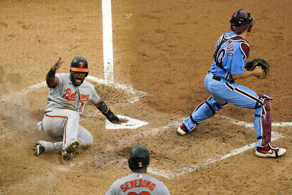 Baltimore Orioles' Hanser Alberto, left, reacts after scoring past Philadelphia Phillies catcher J.T. Realmuto, right, on a three-run double by Anthony Santander during the fifth inning of a baseball game, Thursday, Aug. 13, 2020, in Philadelphia. (AP Photo/Matt Slocum)