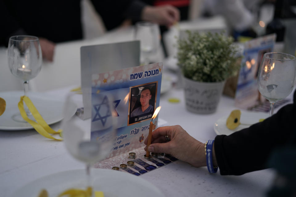 A person lights a candle on a table set for hostages being held in the Gaza Strip by the Hamas militant group during the Jewish holiday of Hanukkah in the Hostages Square at the Museum of Art, in Tel Aviv, Israel, Friday, Dec. 8, 2023. (AP Photo/Leo Correa)