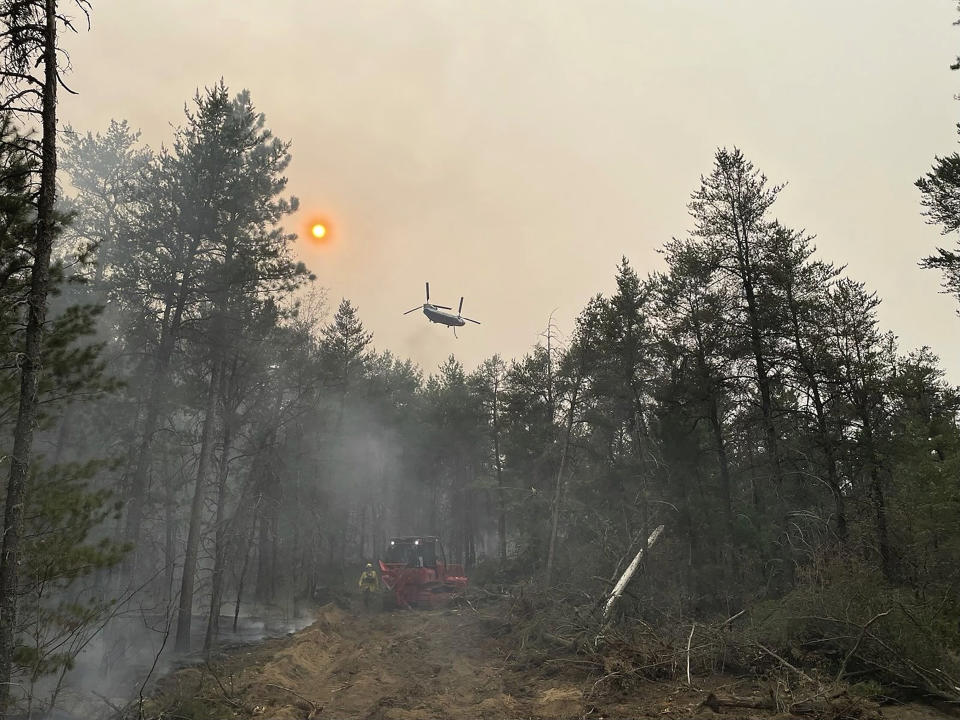 This image provided by the The Michigan Department of Natural Resources shows emergency personnel, aircraft and heavy equipment being used to suppress the wildfire near Grayling, Mich., June 3, 2023, (The Michigan Department of Natural Resources via AP)