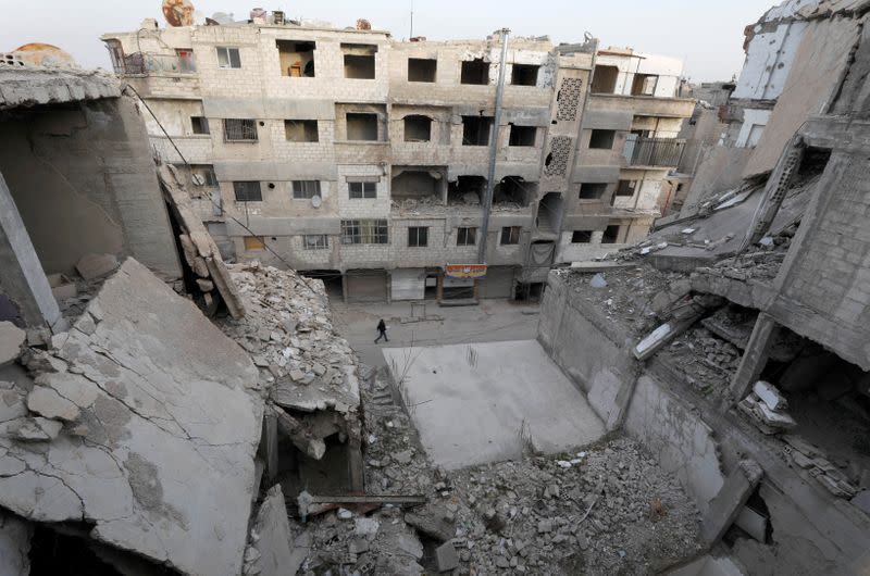 A man walk pasts damaged buildings in Douma
