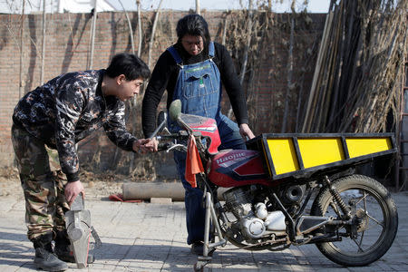 Geng Shuai, dubbed "Useless Edison" by his fans, gets a motorcycle started, that was refitted to transport vegetables for sale, under the help of his brother Geng Da (L), at a yard outside his workshop in Yangcun village of Baoding, Hebei province, China January 22, 2019. REUTERS/Jason Lee