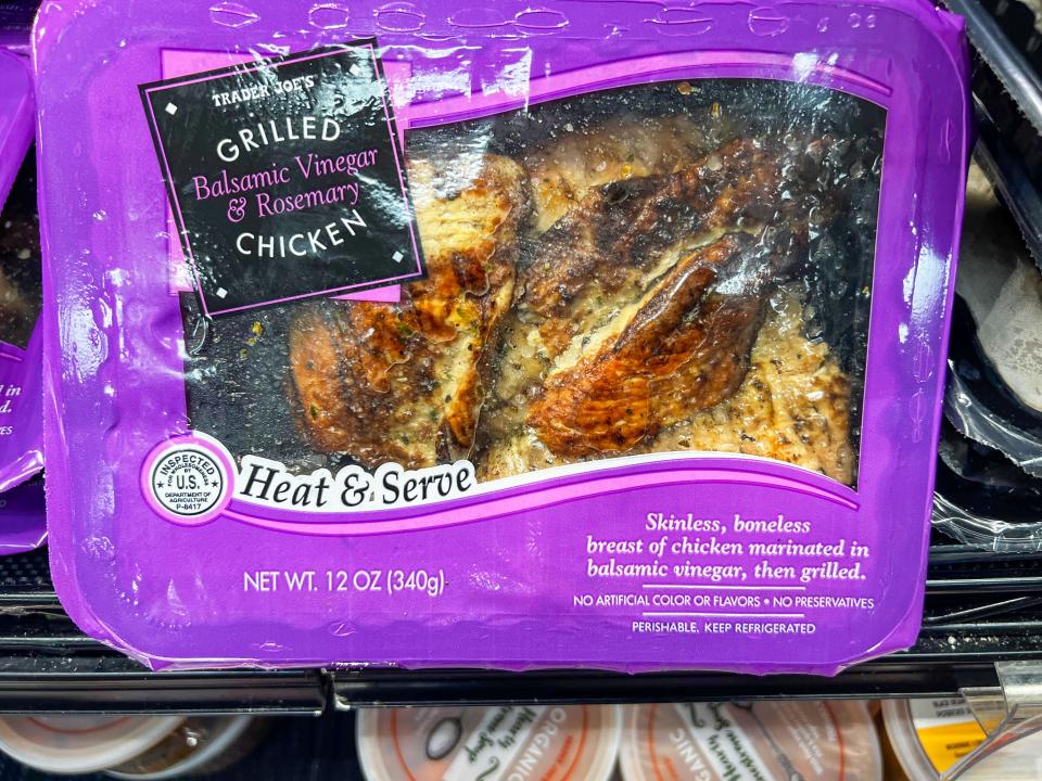A clear container with a purple border and black label reading "grilled balsamic vinegar and rosemary chicken." The package contains grilled chicken breasts