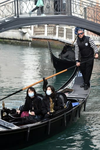 A gondolier steers tourists in facemasks along a canal in Venice