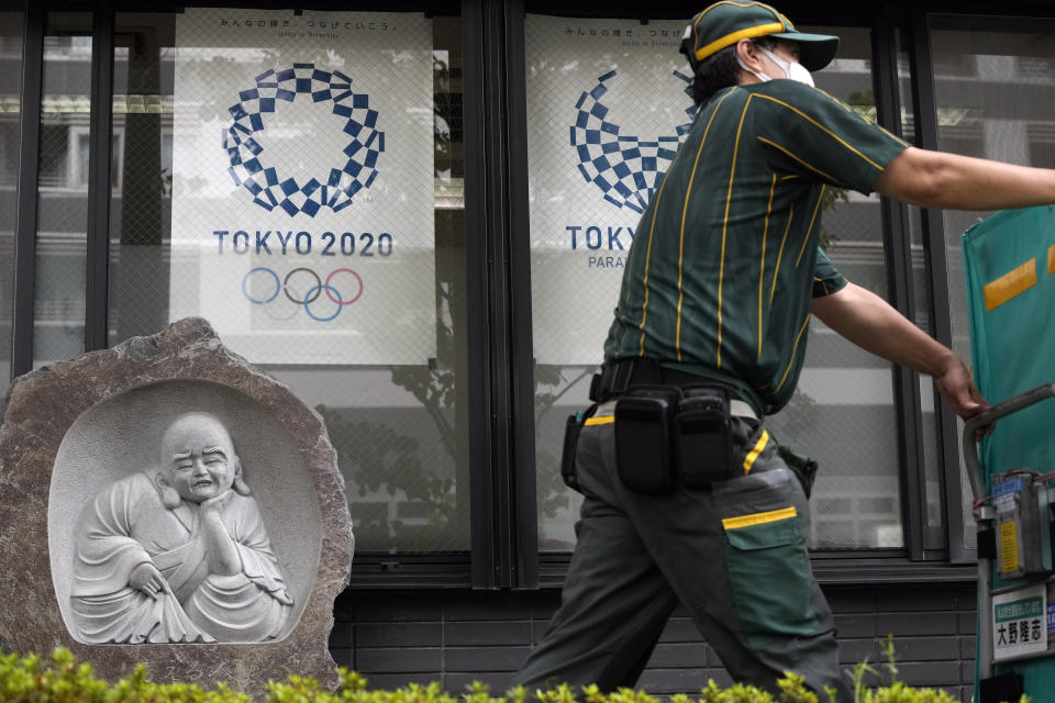 FILE - In this July 13, 2021, file photo, a delivery man pushes a cart full of packages as he passes by a business with Tokyo 2020 Olympics and Paralympics posters displayed on the windows in Tokyo. How are we to judge the pandemic-delayed Tokyo Olympics when they wrap up in two weeks? It's a straightforward question but it's difficult to answer. That's because there are many interests involved. (AP Photo/Kiichiro Sato)