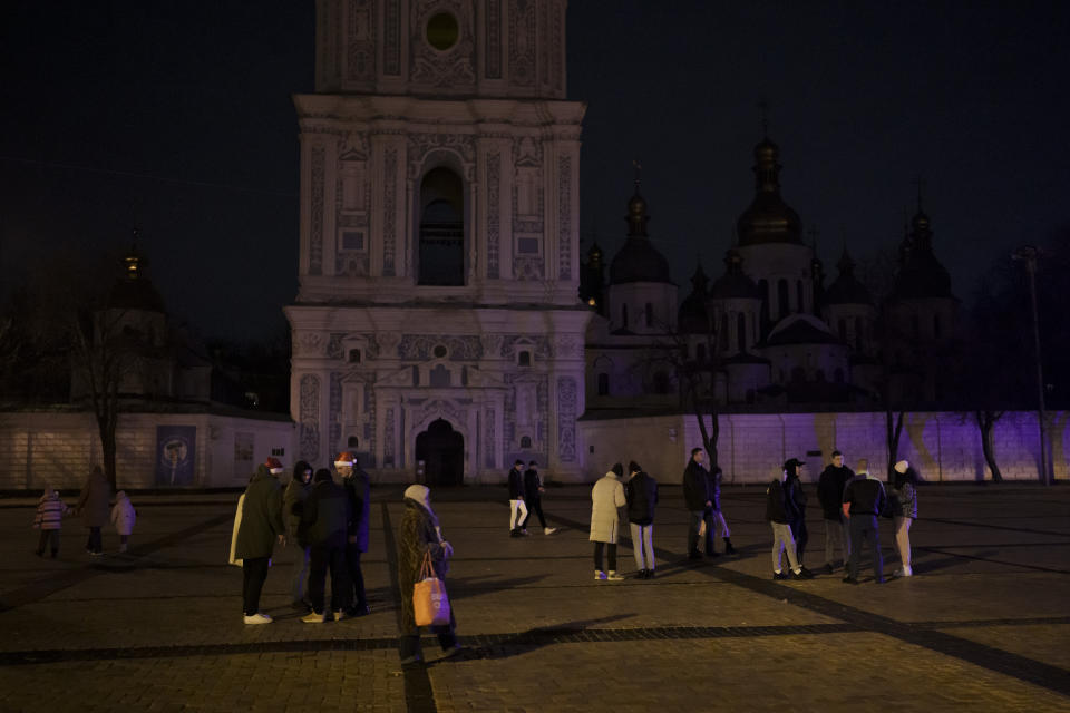 People stand in Sophia Square before curfew on New Year's Eve in Kyiv, Ukraine, Saturday, Dec. 31, 2022. Multiple blasts rocked the capital and other areas of Ukraine on Saturday. (AP Photo/Felipe Dana)