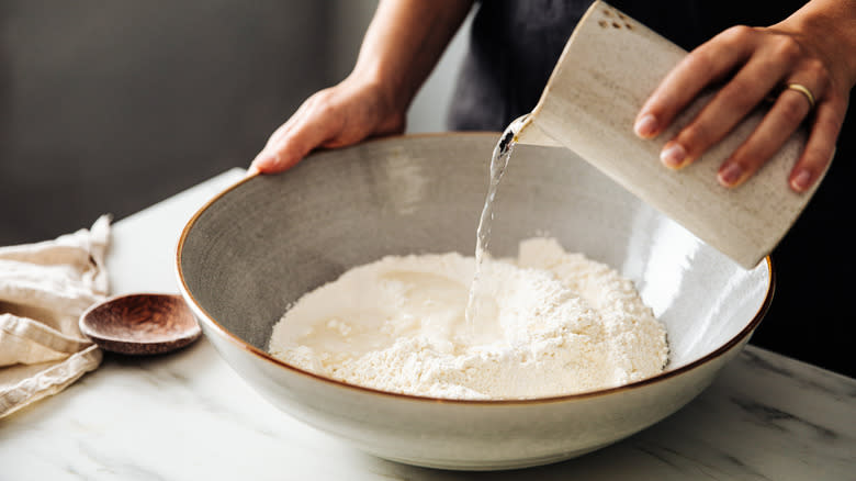 hands pouring water into bowl of flour