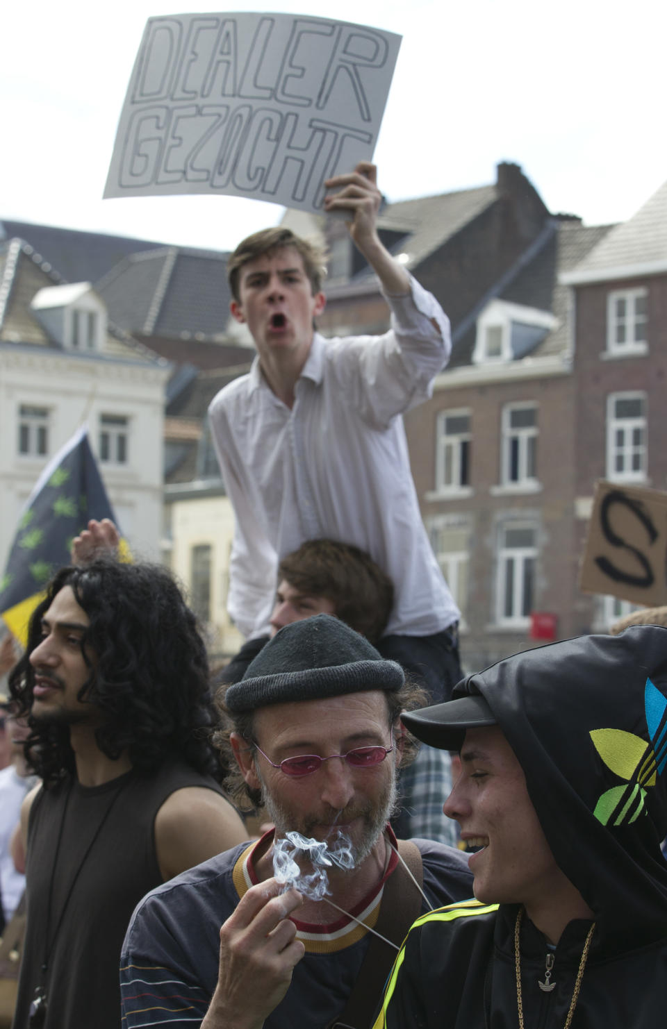 Two people smoke a marijuana joint, bottom, as a demonstrator holds a sign reading "Dealer Wanted" during a protest rally in Maastricht, southern Netherlands, Tuesday May 1, 2012. A policy barring foreign tourists from buying marijuana in the Netherlands goes into effect in parts of the country Tuesday, with a protest planned in the southern city of Maastricht. Weed is technically illegal in the Netherlands, but it is sold openly in small amounts in designated cafes under the country's famed tolerance policy. The government has said that as of May 1, only holders of a "weed pass" will be allowed to purchase the drug, and nonresidents aren't eligible. (AP Photo/Peter Dejong)