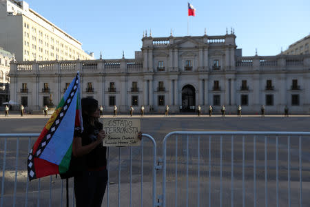 A Mapuche indigenous activist holds up a banner, which reads: 'Terrorist State', outside government house during a protest demanding justice for Camilo Catrillanca, an indigenous Mapuche man who was shot in the head during a police operation, in Santiago, December 20, 2018. REUTERS/Ivan Alvarado