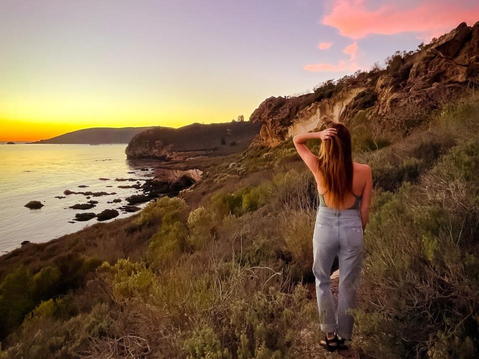Emily walks along a grassy coastline at sunset.