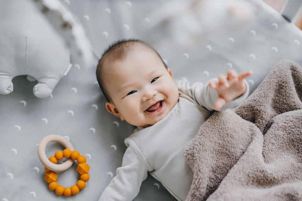 Portrait of a lovely Asian baby girl smiling sweetly while lying on the crib. She is raising her hand trying to touch the cot mobile. Baby's growth and development concept