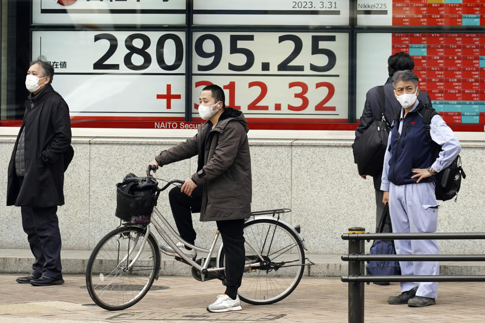People wait for traffic light to change in front of an electronic stock board showing Japan's Nikkei 225 index at a securities firm Friday, March 31, 2023, in Tokyo. Asian stocks followed Wall Street higher Friday ahead of a United States inflation update that traders hope will prompt the Federal Reserve to ease plans for more interest rate hikes. (AP Photo/Eugene Hoshiko)