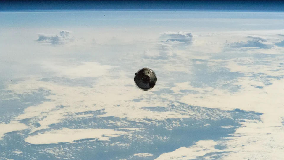 Blick von der ISS auf die sich nähernde Boeing Starliner-Kapsel. Dahinter ist die wolkenverhangene Erde zu sehen.