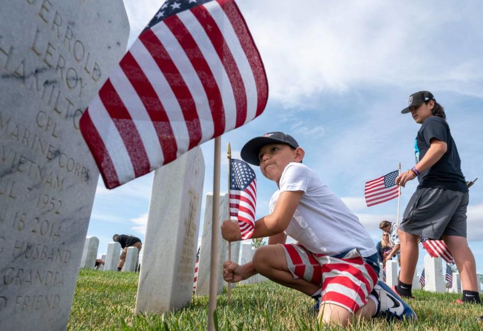 Derrick Garcia, 6, of Winters, uses his might to place a lawn flag as his family, including brother Anthony, 12, right, put flags in front of headstones at the Sacramento Valley National Cemetery in Dixon as part of the Memorial Day ceremony Saturday, May 28, 2022. The ceremony returned to in-person after a two-year COVID-19 hiatus.
