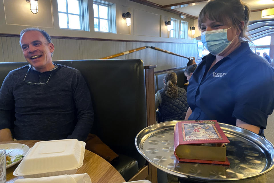 In this Ryan Wasson family photograph, a box of "Santa's Book of Candy" Christmas re-gift is delivered as dessert to Eric Wasson, left, by a waitress on April 17, 2021, in Wolfeboro, N.H. Two New Hampshire brothers have gotten their holiday regifting skills down to an art, and have been passing the same hard candy treats back and forth for over 30 years. Starting in 1987, Ryan Wasson gave the treat to his brother, Eric Wasson, as a joke for Christmas, knowing that Eric wouldn't like it. The Christmas gift was delivered in April 2021 after their family Christmas gathering was delayed in 2020 due to the COVID-19 virus outbreak. (Ryan Wasson family photograph via AP)