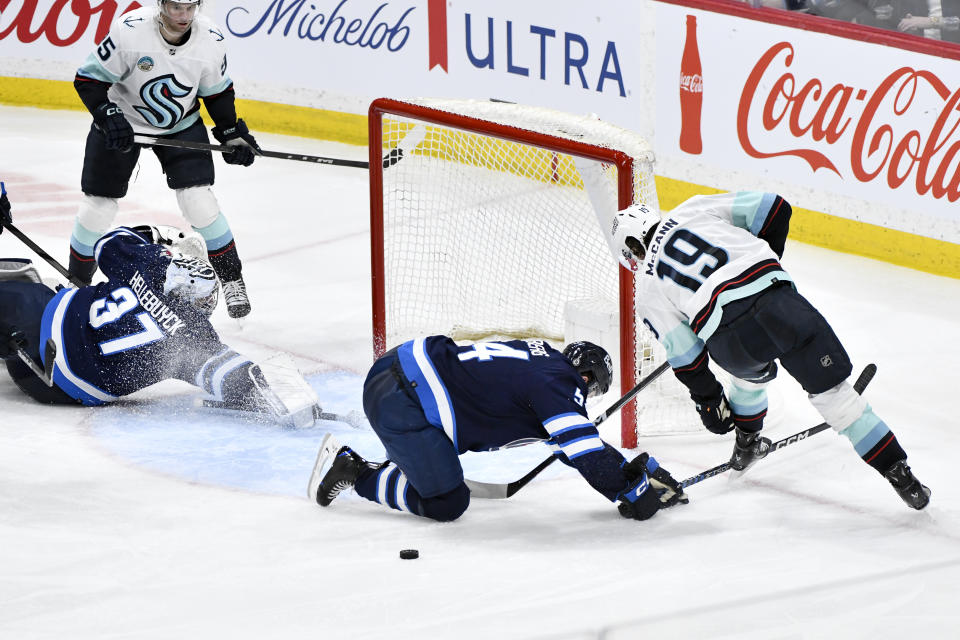 Winnipeg Jets' Dylan Samberg (54) checks Seattle Kraken's Jared McCann (19) as he tries to get control of a loose puck behind goaltender Connor Hellebuyck (37) during the third period of an NHL hockey game in Winnipeg, Manitoba on Tuesday April 16, 2024. (Fred Greenslade/The Canadian Press via AP)