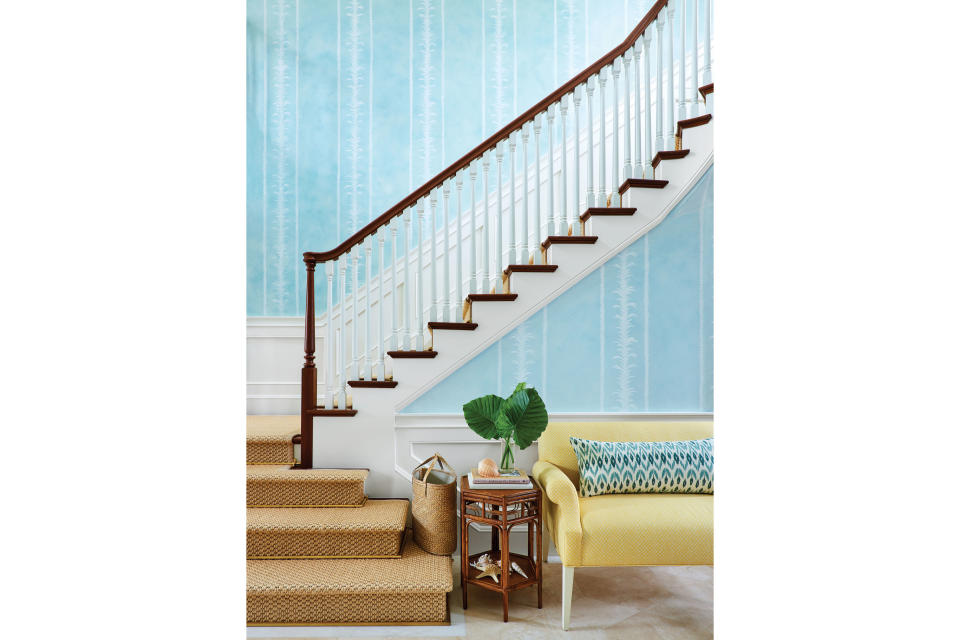 <p>Grand entry stairs are practically de rigueur in Old Palm Beach, but Sharpe updated the architectural standard in the entry with glazed aquamarine walls. “The hue is very similar to the color of the ocean here,” says Sharpe, who added a vertical, hand-painted acanthus leaf pattern, which helps elongate the space. A sunshine yellow sofa is a reminder of fair skies outdoors, and the side table delivers another quintessential local design detail: rattan. The flooring is travertine in a cut-star pattern, and the seating fabric is by <a href="http://quadrillefabrics.com/chinaseas.html" rel="nofollow noopener" target="_blank" data-ylk="slk:China Seas;elm:context_link;itc:0;sec:content-canvas" class="link ">China Seas</a>.</p>