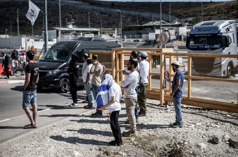 Israelis stand near the site where humanitarian aid trucks were vandalized near the Tarqumiya Checkpoint, on their way to the Gaza Strip. Ilia Yefimovich/dpa