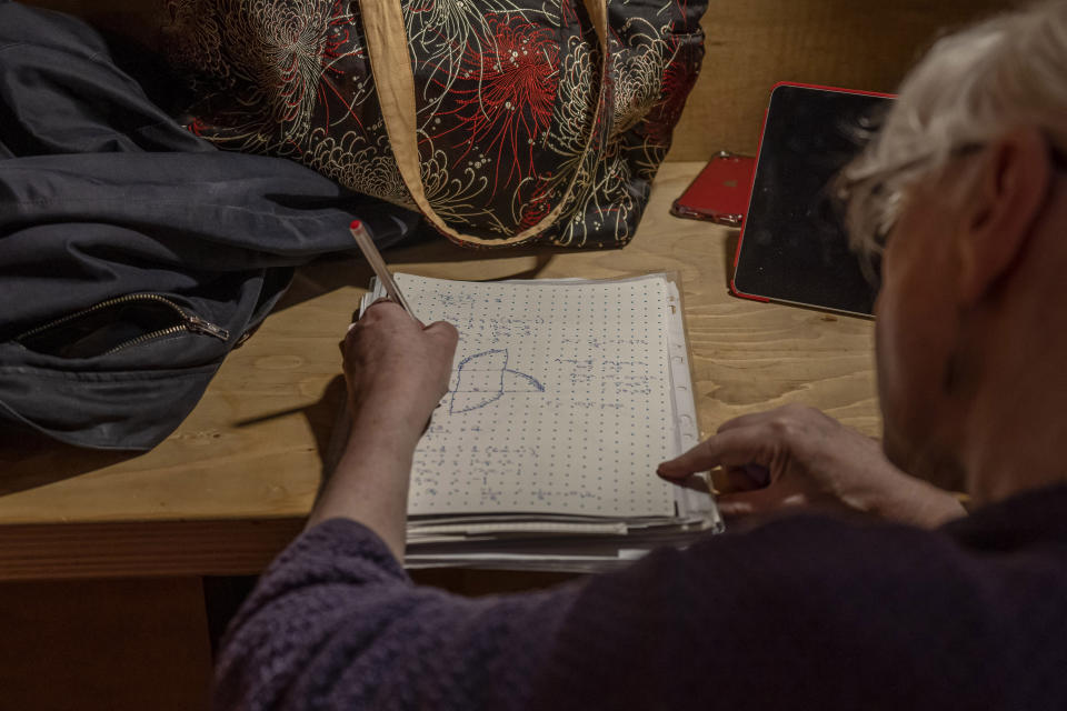 Anne Bolger works on her math at the Other Place theater, in Stratford-upon-Avon, Warwickshire, England, Tuesday, Feb. 28, 2023. The foyer of the Other Place theater in Shakespeare's birthplace of Stratford-upon-Avon is a cozy refuge from winter. One day a week the theater becomes a "warm hub," set up by the Royal Shakespeare Company to welcome people who may be struggling to heat their homes because of sky-high energy prices. (AP Photo/Kin Cheung)