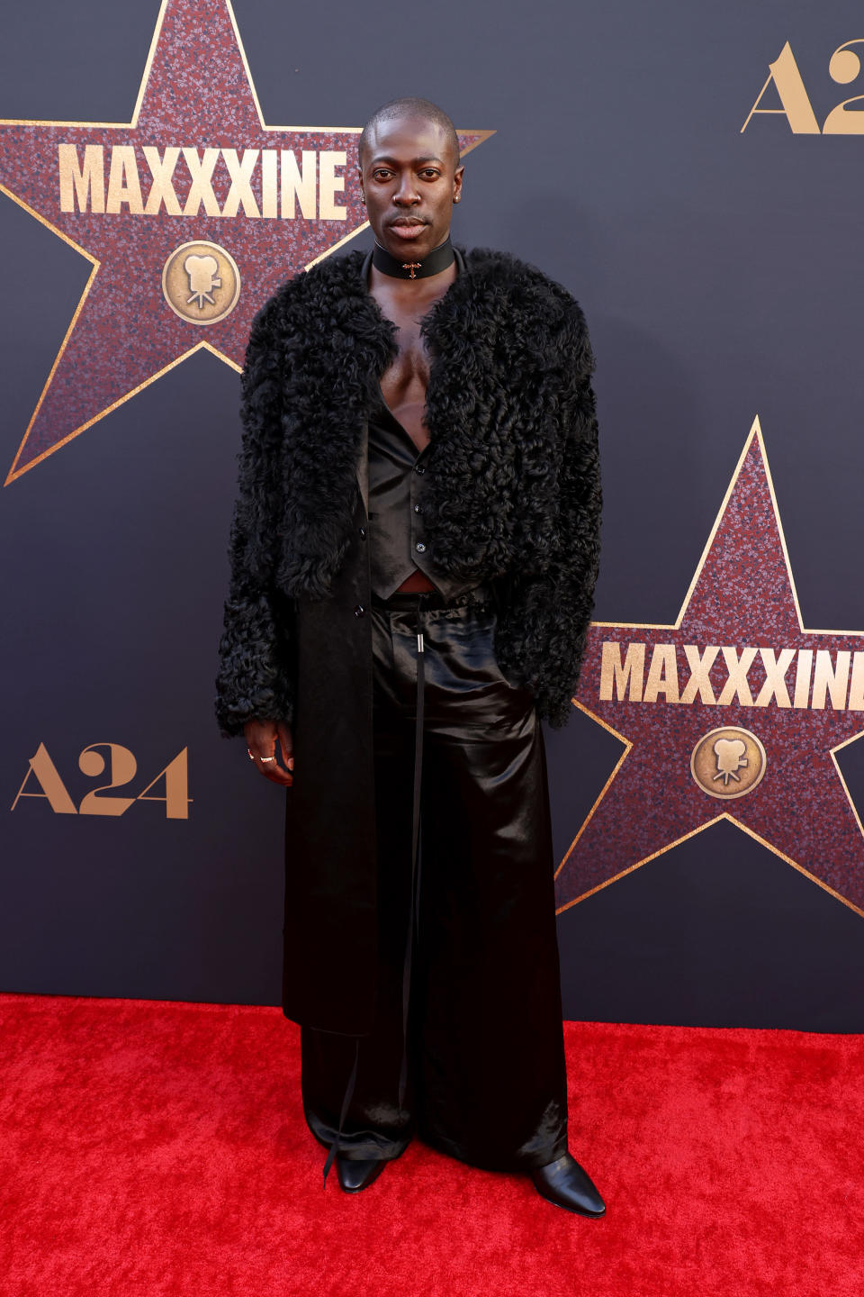 Moses Sumney is wearing a black textured coat, leather pants, and a choker necklace