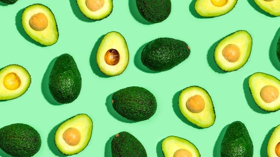 Whole and halved avocadoes on a green table top