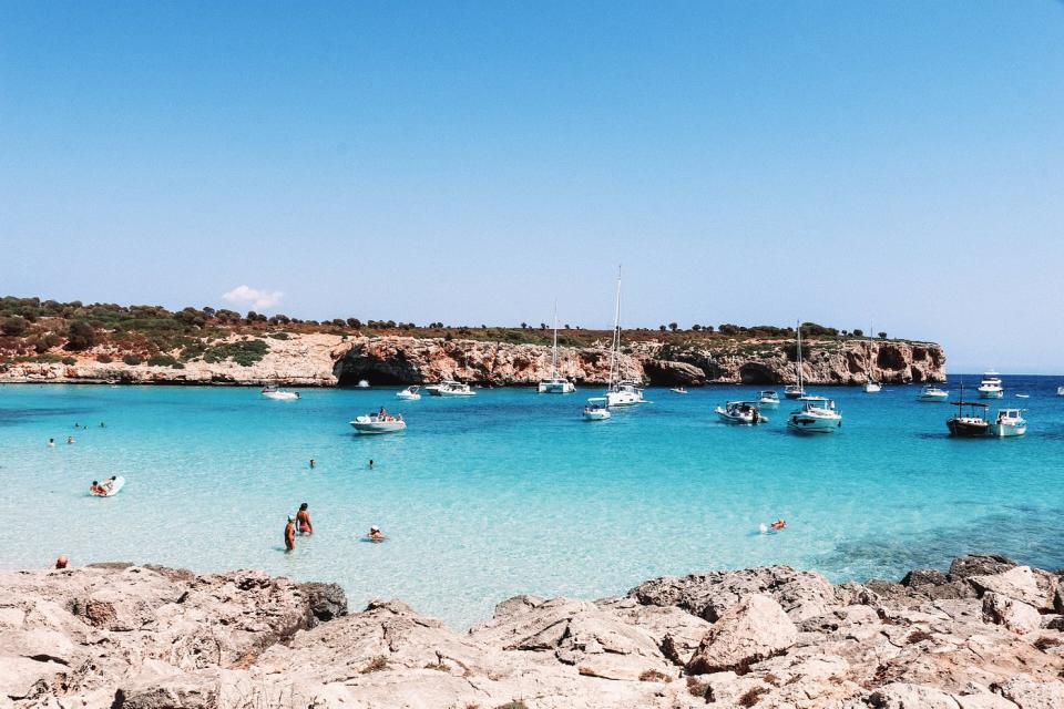 Crystal blue water with boats and people swimming and rocky headlands in Majorca, Balearic Islands