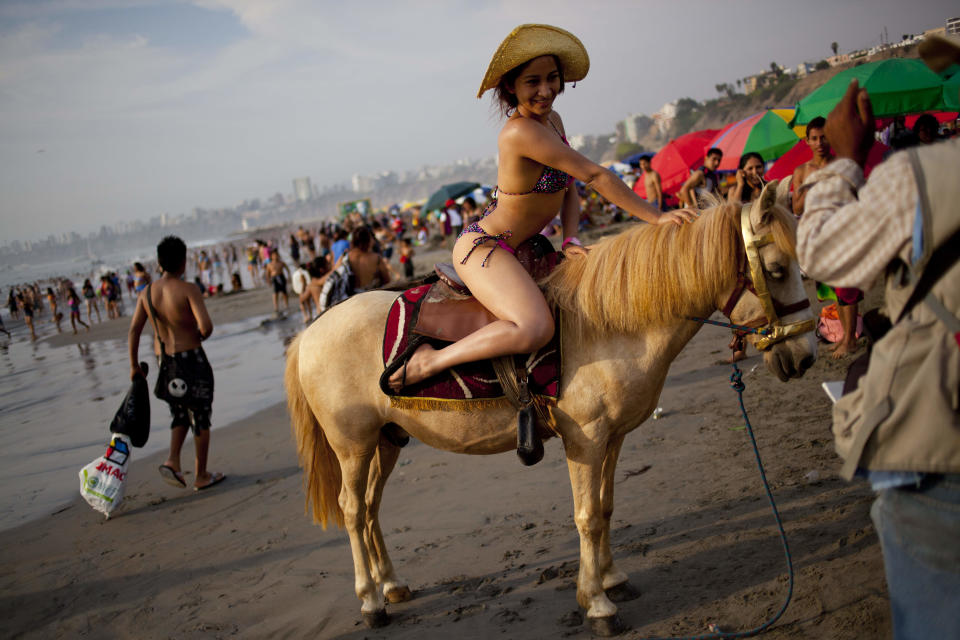In this March 3, 2013 photo, Adela Cabrera, 19, poses for a picture on a horse at Agua Dulce beach in Lima, Peru. For five Peruvian soles or about two U.S. dollars beachgoers can pose for a photo to record their day at the beach, in front of backdrops of their choice that include forest landscapes, exotic beach scenes or atop horses. While Lima's elite spends its summer weekends in gate beach enclaves south of the Peruvian capital, the working class jams by the thousands on a single municipal beach of grayish-brown sands and gentle waves. (AP Photo/Rodrigo Abd)