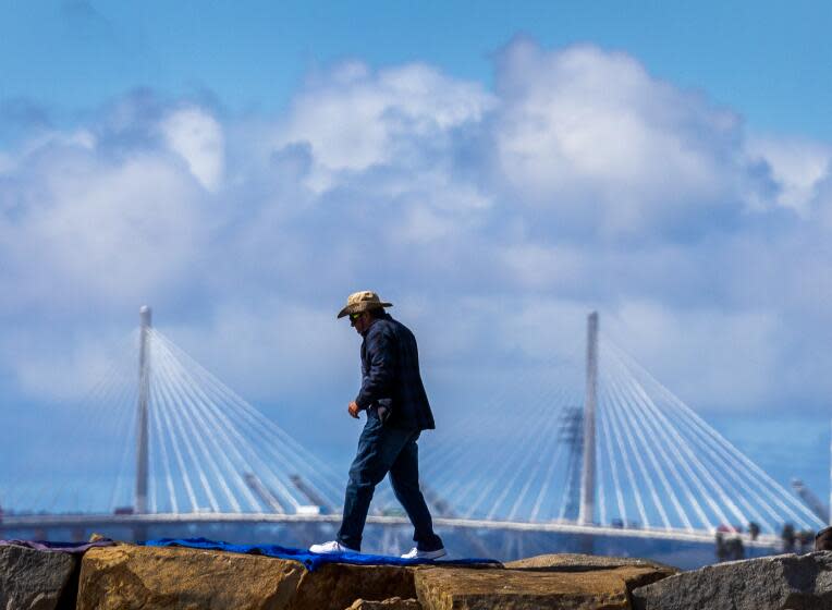 Long Beach, CA - February 21: As the storm passes through Southern California, a man takes a scenic walk on the jetty that separates Los Alamitos bay and the San Gabriel River with a view of clouds and the Long Beach International Gateway Bridge in Long Beach Wednesday, Feb. 21, 2024. (Allen J. Schaben / Los Angeles Times)