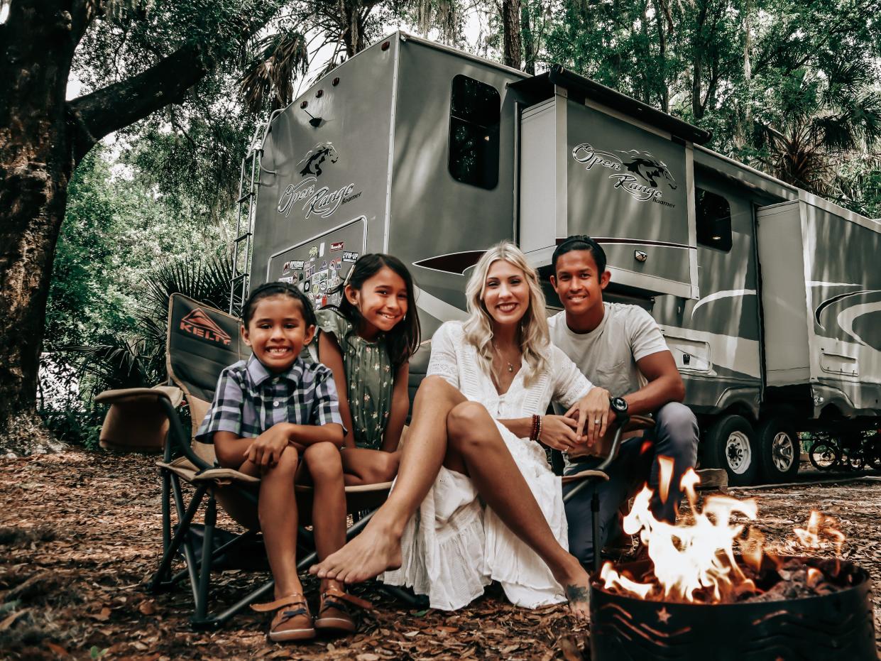 Family of four by campfire with large RV home in the background