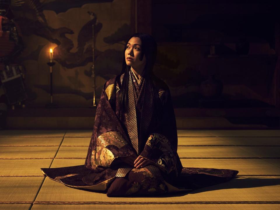fumi nikaido as ochiba no kata, a woman wearing ornatedeep purple robes and looking up towards a patch of sun