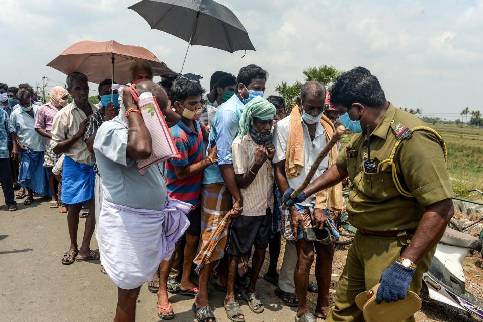 A policeman (R) holding a stick regulates the crowd as people line up to buy alcohol at a liquor shop after the government eased a nationwide lockdown imposed as a preventive measure against the COVID-19 coronavirus, on the outskirts of Chennai on May 7, 2020. (Photo by Arun SANKAR / AFP) (Photo by ARUN SANKAR/AFP via Getty Images)