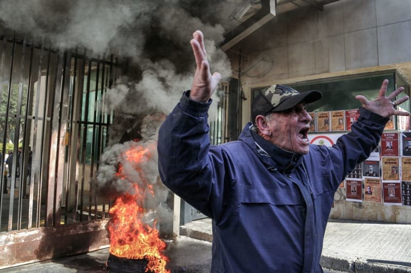 A Lebanese depositor chants slogan in front of burning tyres outside a local bank, during a protest to demand the imposition of a timetable for returning the savings of depositors. The protests of depositors against banks has been expressed regularly since the restrictions imposed by the Lebanese banks in 2019, at the start of an unprecedented economic crisis in which Lebanon is still entangled. Marwan Naamani/dpa