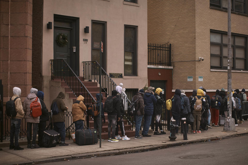 FILE - Migrants queue in the cold as they look for a shelter outside a migrant assistance center at St. Brigid Elementary School on Tuesday, Dec. 5, 2023, in New York. Nervous officials in suburbs and outlying cities near Chicago and New York are giving migrants arriving from the southern border a cold shoulder. Edison, New Jersey, the mayor warned he would send people back to the border if they came to his city in buses. The moves come amid attempts to circumvent new limits on dropping migrants in the two cities, opening a new front in response to efforts led by Texas Gov. Greg Abbott to pay for migrants to leave his state. (AP Photo/Andres Kudacki, File)