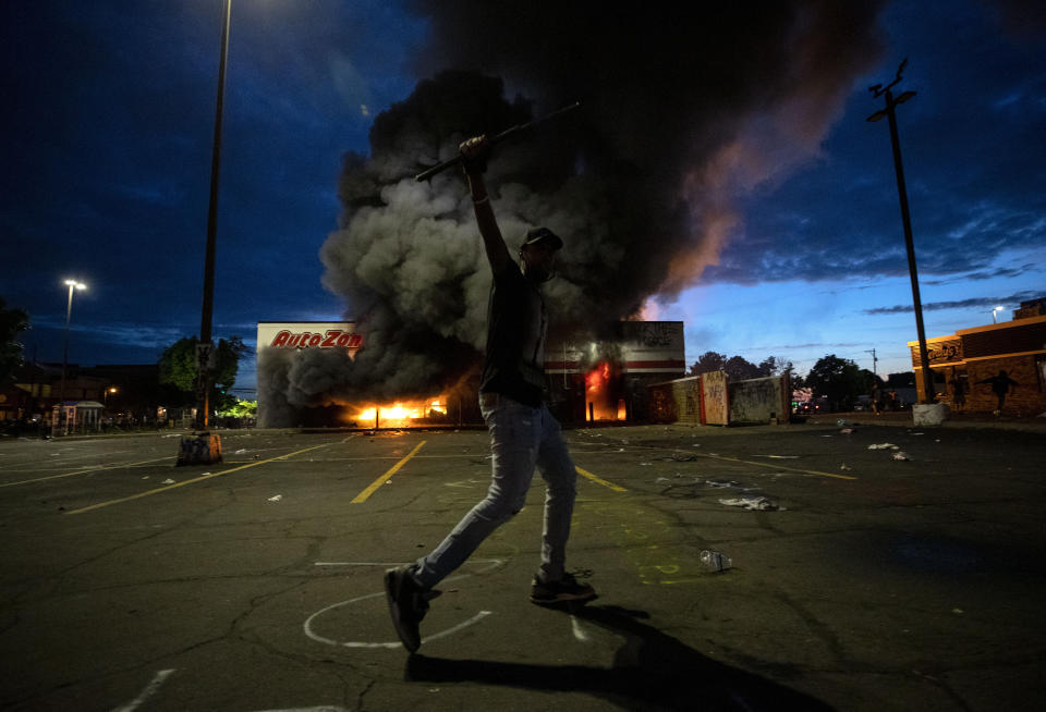 A man poses for a photo in the parking lot of an AutoZone store in flames, while protesters hold a rally for George Floyd in Minneapolis on Wednesday.  (Photo: ASSOCIATED PRESS)